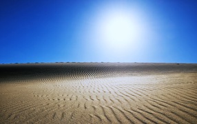 Wavy sand in the desert under the scorching sun in the blue sky