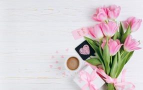 Букет розовых тюльпанов на столе с чашкой кофе и подарком 
