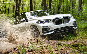 White BMW X5 SUV rides through the mud in the woods  