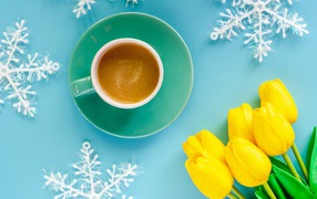 A cup of coffee on a blue background with snowflakes and a bouquet of yellow tulips