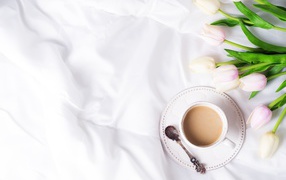 Чашка кофе на белом покрывале с тюльпанами
