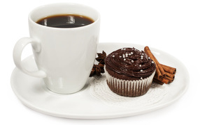 A cup of coffee on a white plate with a cupcake and cinnamon
