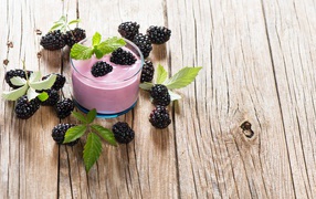 Стакан йогурта на деревянном столе с ягодами ежевики