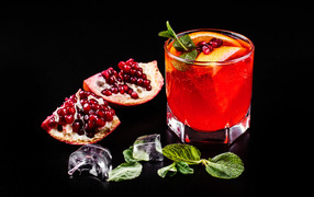 Alcoholic drink in a glass on a black background with pomegranate, ice cubes and mint