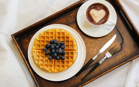 Cappuccino in a cup on a tray with waffles and blueberries