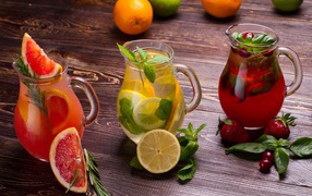 Три стеклянных графина с напитком на деревянном столе с фруктами