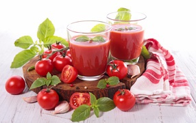 Два стакана томатного сока на столе с помидорами и зеленью 