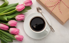Белая чашка кофе на столе букетом розовых тюльпанов и подарком