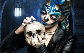 Girl with a make-up on the face with a skull in his hands on Halloween