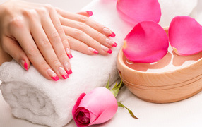 Women's hands with a beautiful manicure lie on a white towel on the table with a rose