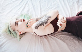The girl with a tattoo on her arm is lying on the bed
