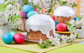 Красивый кулич с белой глазурью на столе с крашеными яйцами и веточками цветущей вишни