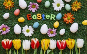 Надпись Easter на зеленой траве с крашеными яйцами и цветами