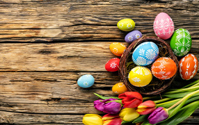 Крашеные пасхальные яйца с букетом тюльпанов на деревянном фоне