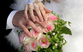 Hands of the bride and groom on the bouquet with pink roses