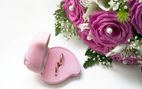 Two wedding rings in a box on a white background with a bouquet of roses