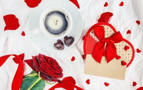 A cup of coffee on the table with a box in the shape of a heart and a red rose for the beloved