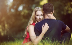 Beautiful girl hugging a guy sitting on the grass
