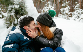 Couple in love sitting under a snowy fir branch in winter