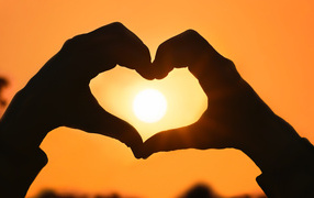 Heart with hands on a background of the sun in the sky