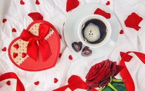 Mug with coffee and chocolates on a table with a gift and a red rose