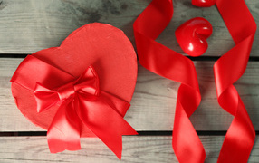 Красная коробка в форме сердца на деревянном столе с красными лентами