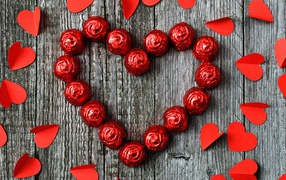 Red heart made of chocolates on a wooden background with paper hearts