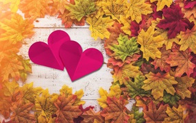 Two red hearts on a table with yellow leaves