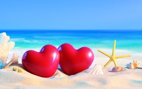 Two red hearts on white sand with shells on a background of the sea