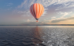 Big orange balloon in the sky over calm water.