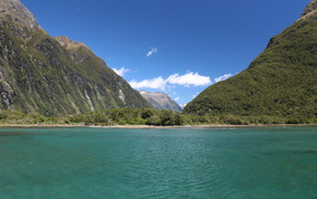 Blue water in the lake on the background of green-covered mountains under a blue sky