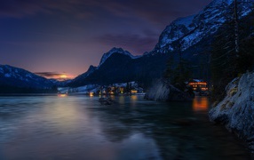 Город у озера на фоне заснеженных гор ночью 