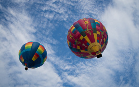 Two large balloons in the blue sky with white clouds