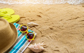Hat, glasses, towel and shells on the yellow sand by the sea