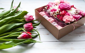 Букет розовых тюльпанов на столе с коробкой печенья макарон и цветами