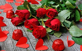 Букет красных роз на деревянном столе с конфетами и красными сердечками