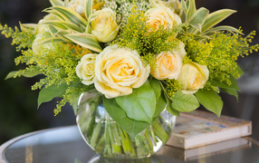 Красивый букет роз с зелеными листьями в в вазе на стеклянном столе