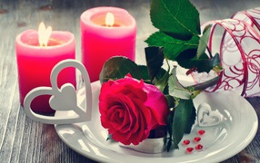 Красная роза на белой тарелке с сердечками на столе с зажженными свечами