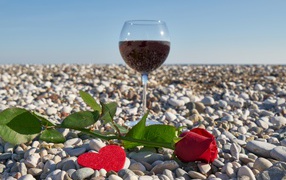 Red rose on sea pebbles with a heart and a glass of wine