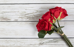 Three artificial red roses on a wooden background
