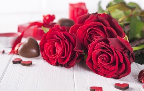 Три красивые красные розы на столе с конфетами
