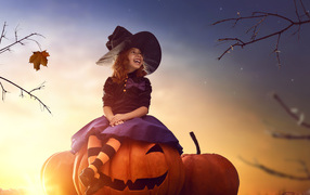 Улыбающаяся девочка сидит на тыкве в костюме на Хэллоуин 