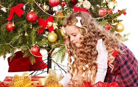Красивая маленькая девочка смотрит подарки под елкой на новый год 