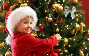Мальчик в шапке Санта Клауса наряжает елку