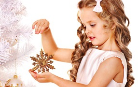Маленькая девочка держит елочную игрушку снежинку в руке
