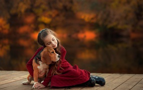 Little girl hugs a beagle dog on the bridge