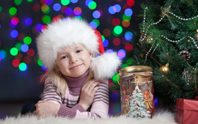 Маленькая девочка в новогодней шапке у елки