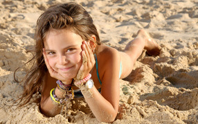 Маленькая девочка лежит на песке на пляже