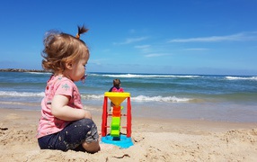 Маленькая девочка играет на песке у моря
