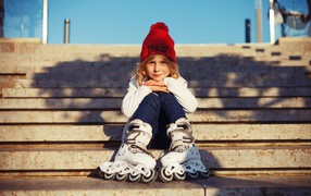 Маленькая девочка в роликах сидит на ступеньках 